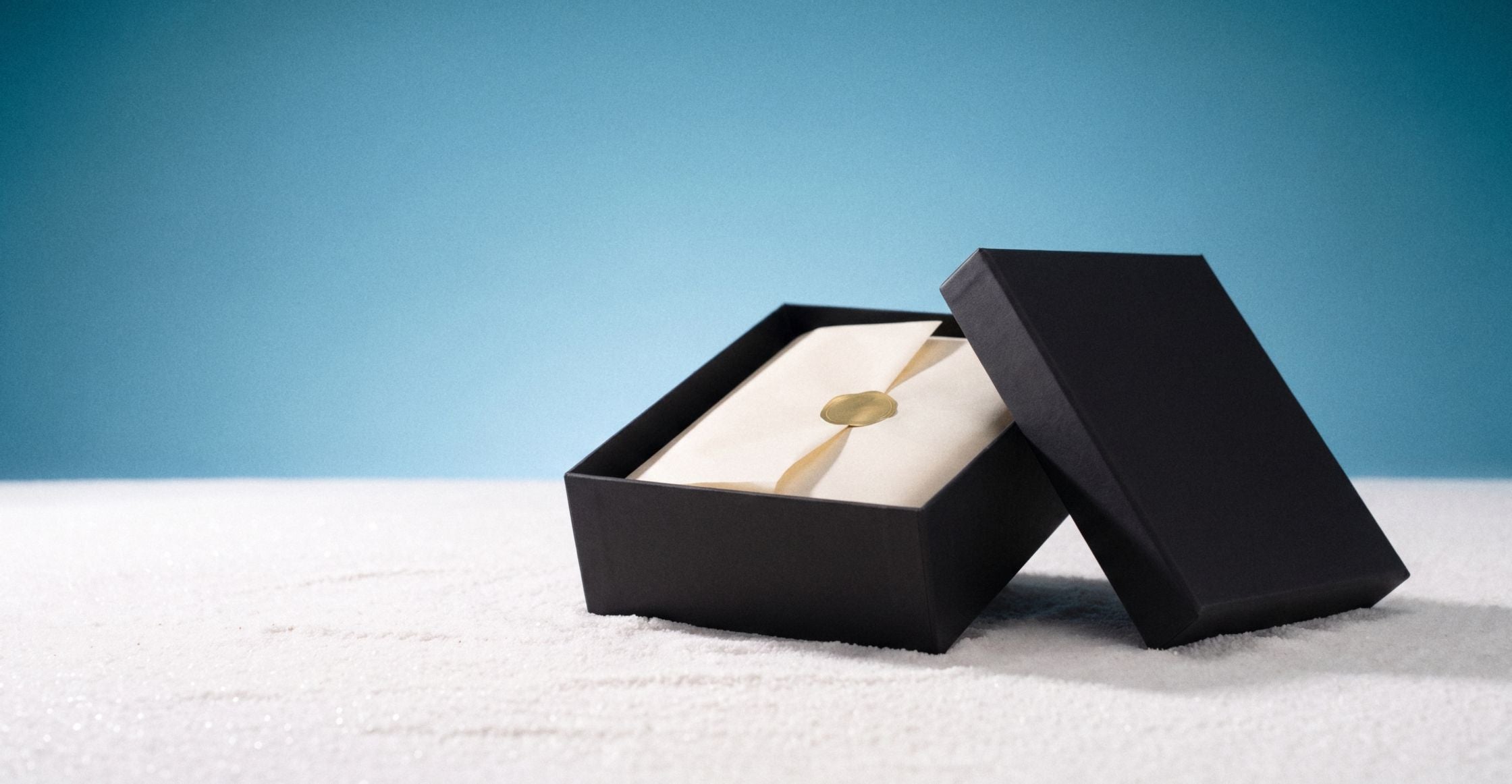 An open black gift box with a gold wax seal on a blue studio plate