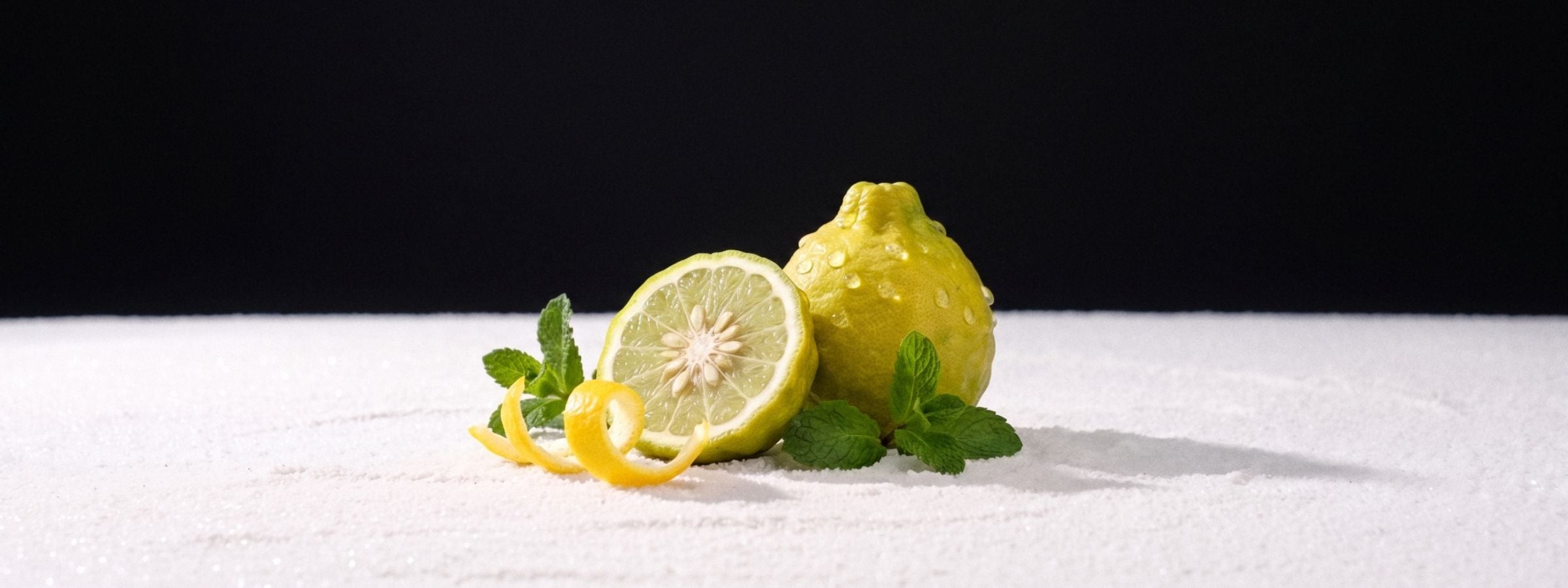 Bergamot, lemon peel and mint on a white salt floor against a black studio backdrop