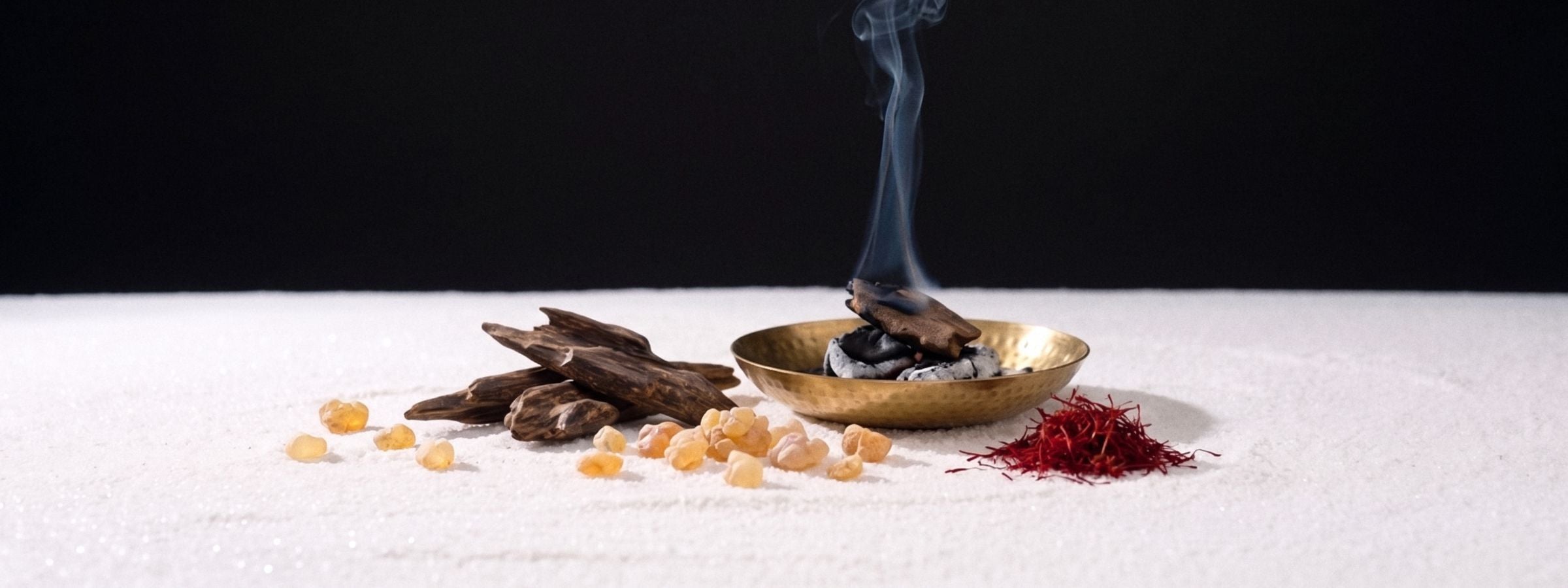 Oud wood, resin and saffron beside a smoking brass dish on a black studio plate